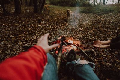 Low section of man sitting by campfire in forest
