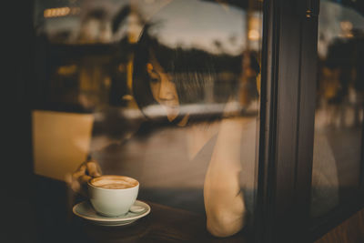 Young woman having coffee at cafe seen through window