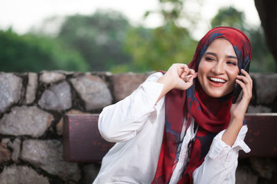 Cheerful young woman wearing hijab while talking on smart phone