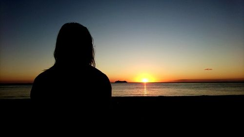 Rear view of silhouette woman sitting on beach at sunset