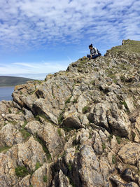 Low angle view of man sitting on rock against sky