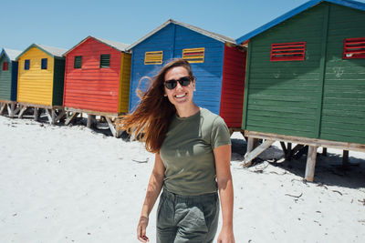 Portrait of smiling young woman standing against beach huts