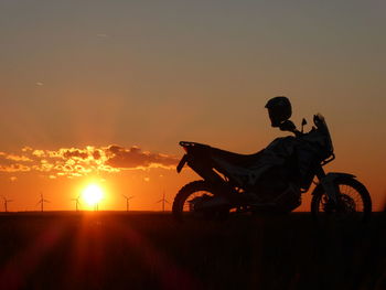 Silhouette people riding bicycle against sky during sunset