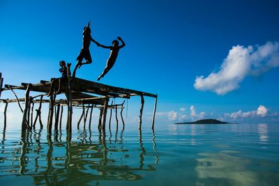 Children on wooden plank jumping in sea