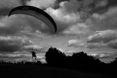 Silhouette people paragliding over field against cloudy sky during sunset