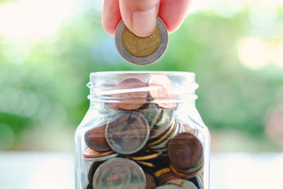 Cropped hand inserting coin in jar