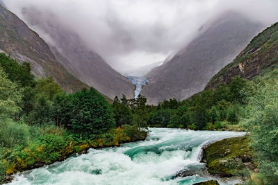 Scenic view of stream amidst trees and mountains against sky