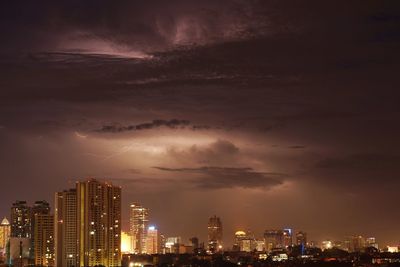Illuminated cityscape against cloudy sky