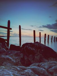 Wooden posts in sea against sky during sunset