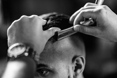 Cropped image of barber shaving man hair in shop