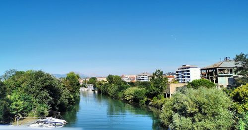 River amidst trees and buildings against clear blue sky