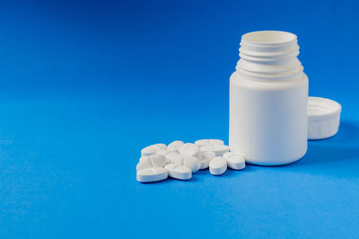 Close-up of pills spilling from bottle against blue background