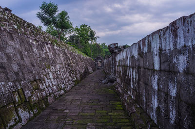 Footpath amidst old wall against cloudy sky