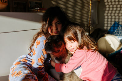 Children hugging their dog sitting altogether in the bed