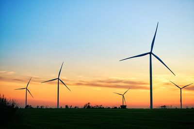 Wind turbines on field against sky during sunset