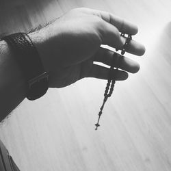 Cropped hand of man holding rosary over hardwood floor