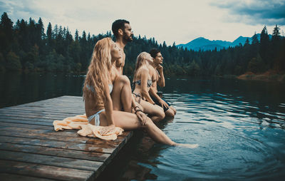 Woman sitting by lake against trees