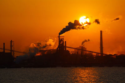 Silhouette smoke emitting from factory against sky during sunset