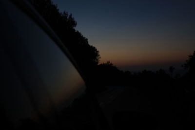 Silhouette trees by road against sky at sunset