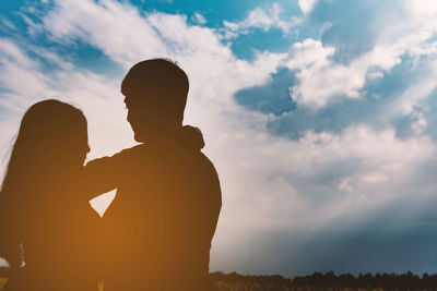 Silhouette couple embracing against cloudy sky during sunset