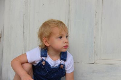 Cute boy looking away while sitting against wall