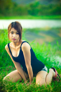 Portrait of young woman kneeling on grassy field