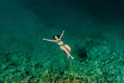Aerial of woman floating on back in crystal clear water relaxing on vacation.