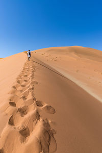 Woman walking on desert against clear sky