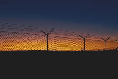 Silhouette fence against sky during sunset