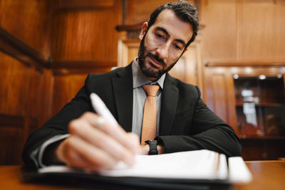 Confident male financial advisor signing contract document in board room during meeting