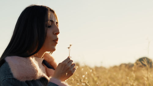 Close up of girl blowing dandelion at sunset