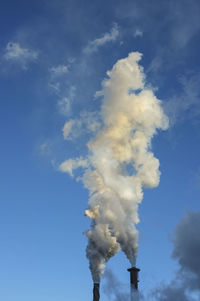 Low angle view of smoke emitting from chimney against blue sky