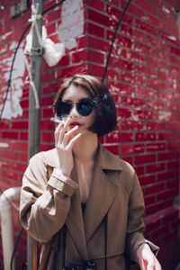Young woman wearing sunglasses standing against brick wall
