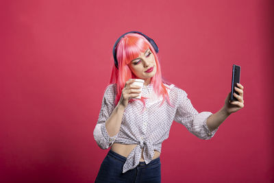 Young woman taking selfie with smart phone while standing against yellow background