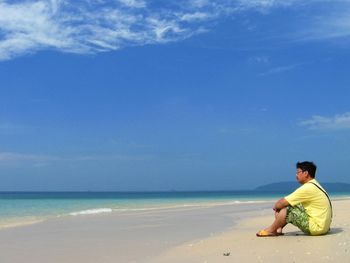 Side view of man resting on shore at beach against sky