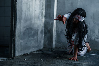 Spooky woman gesturing against wall in abandoned building