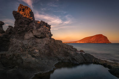 Rock formation in sea against sky during sunset