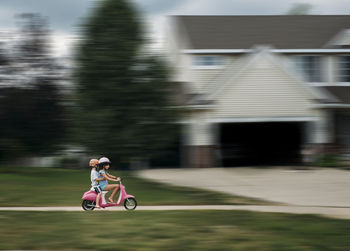 Side view of siblings riding moped scooter at driveway