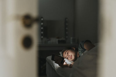 Girl using smart phone while lying on bed in bedroom