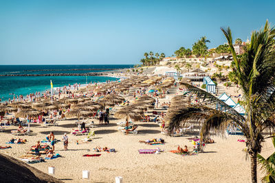 People at beach against clear blue sky