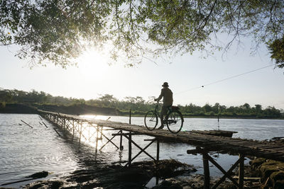 Man riding bicycle by river against sky