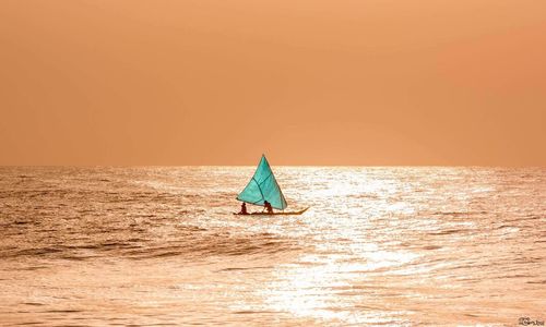 Sailboat sailing on sea against clear sky during sunset