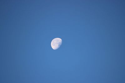 Low angle view of half moon against clear blue sky