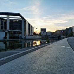 Road by buildings against sky during sunset in city