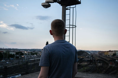 Rear view of man standing in city against sky during sunset