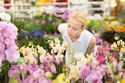 Woman standing by flowering plants at greenhouse