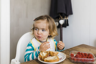 Thoughtful girl eating food on table at home