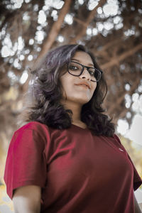 Low angle view portrait of young woman standing against trees