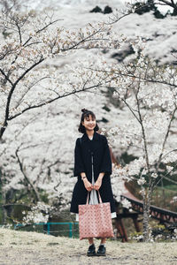 Full length of woman standing against cherry blossom trees