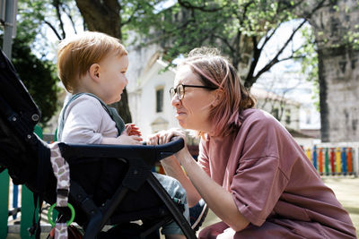 Mother making faces looking at son sitting in baby stroller